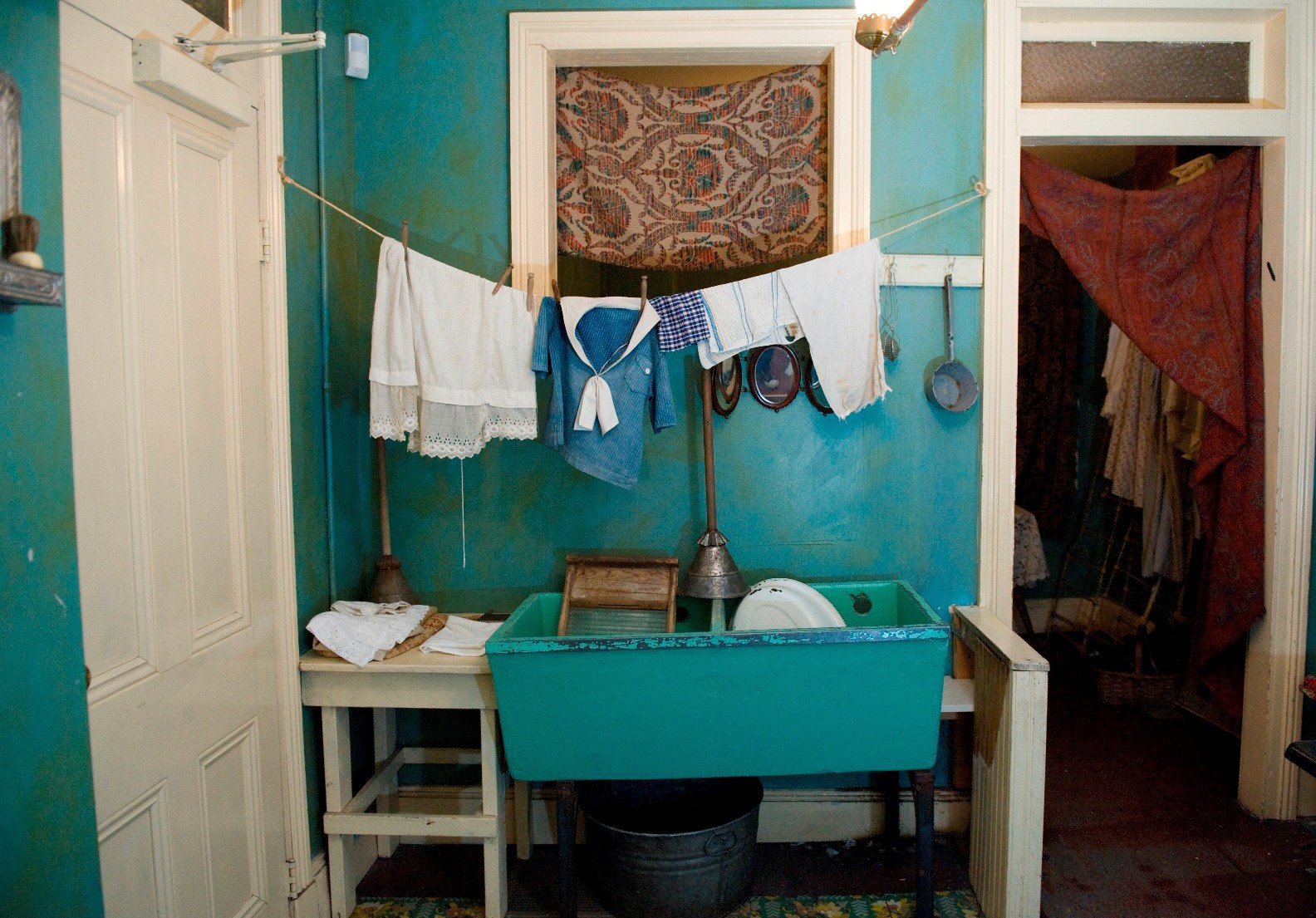 Color photo of a part of the Confino family kitchen with bright blue walls, a blue sink with a washboard inside, and a line of laundry hanging above