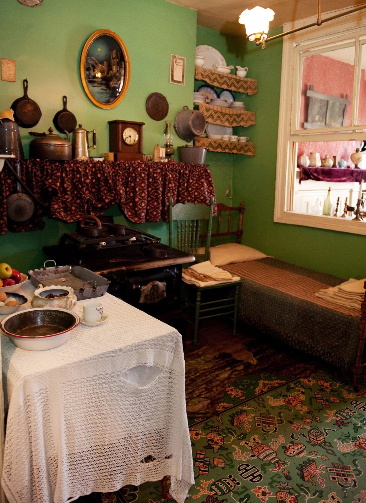 Color photo of the Rogarshevsky family kitchen at 97 Orchard Street where cookware sits on a ledge above a stove nestled between a small bed, chair, and table.