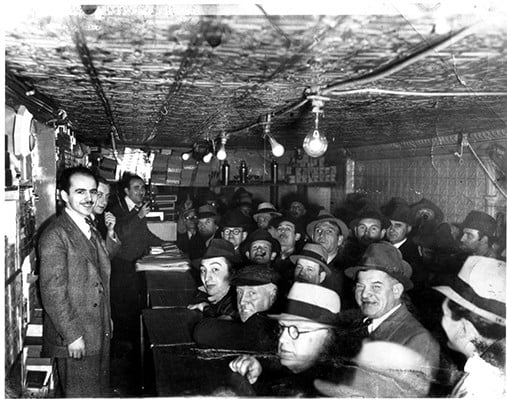Black and white photo of Max Marcus' auction house. The space is small and crowded with adults sitting together and rows of lights hanging above