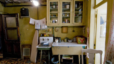 Baldizzi family kitchen with yellow walls and shelves flled with common pantry products beside a line of towels hanging above a countertop and sink