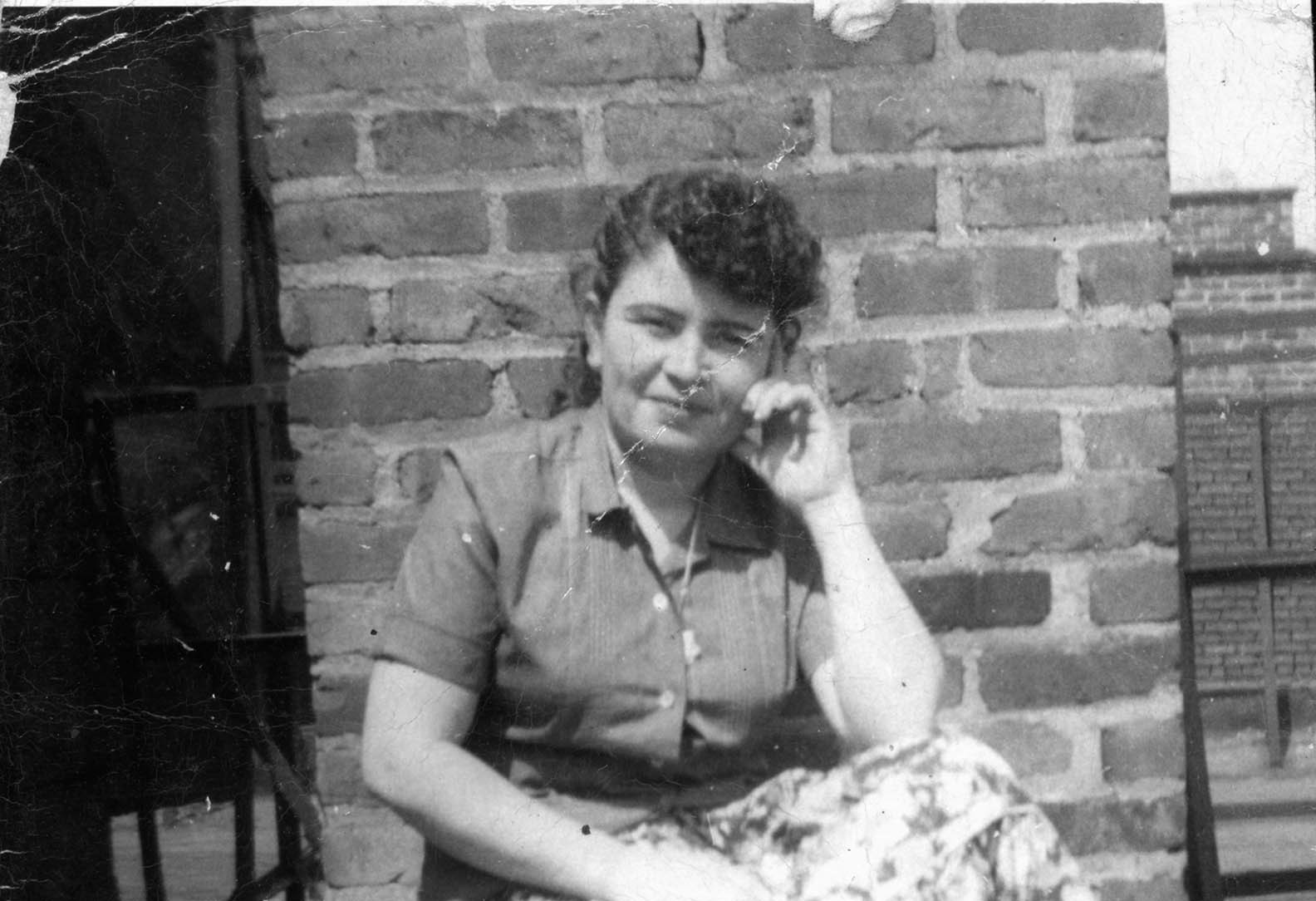 Ramonita Suarez, circa 1970, in a floral skirt and collared shirt posed with her hand on her cheek sitting on the rooftop of 103 Orchard Street