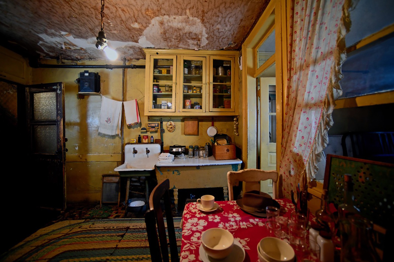 View of the Baldizzi's kitchen showing a table with a red tablecloth and four chairs and a counter, sink, and cabinets on the far wall