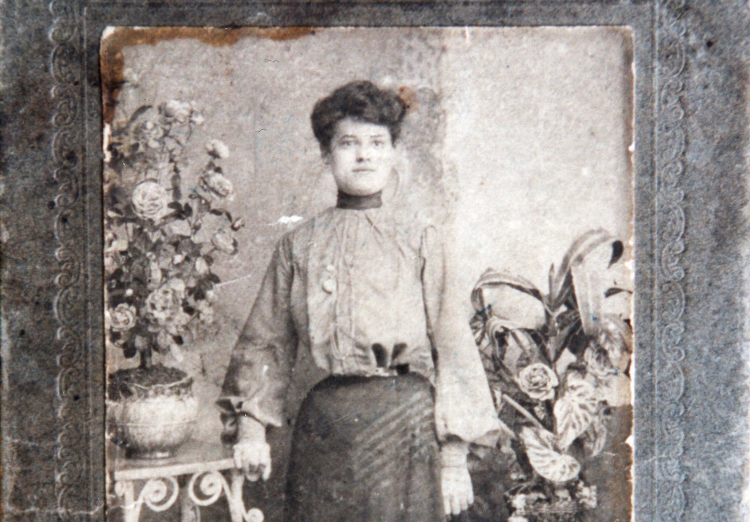 Former 97 Orchard Resident Sarah Burinescu, an adult woman with light-skin tone, in a long-sleeved dress and hair styled in an up-do posing beside a flower vase
