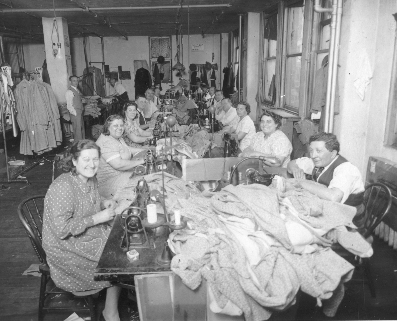 Garment factory in the 1940s with two rows of adults pictured smiling while working at their sewing stations