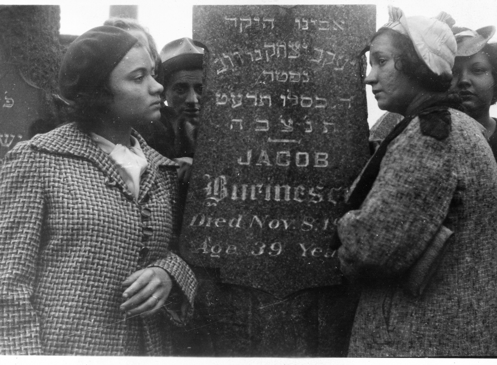 Black and white photo of Jacob Burinescu's family standing on either side of his tombstone