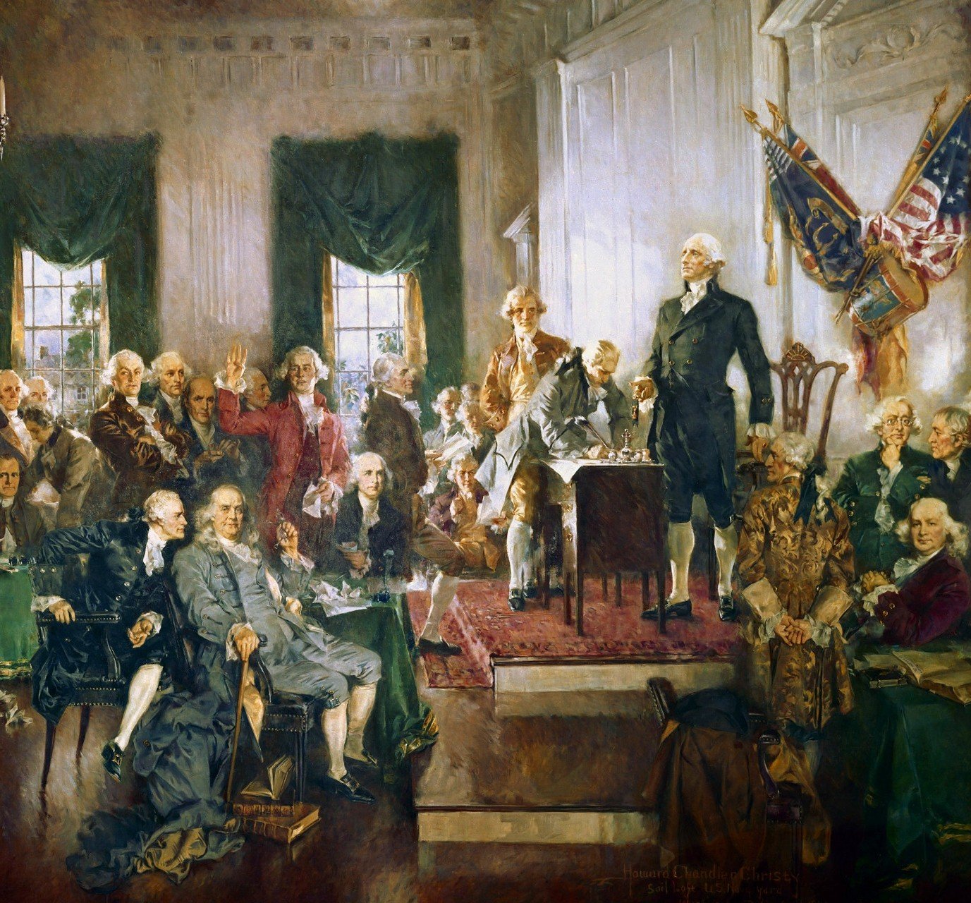 George Washington looks out over a crowd, with an American flag behind him and the Constitution on a desk in front of him being signed by a delegate