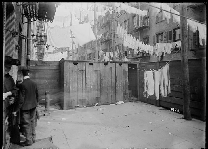Rear yard in 1902 with four outhouses adjacent to each other in an open area and multiple rows of laundry hanging on clothing lines