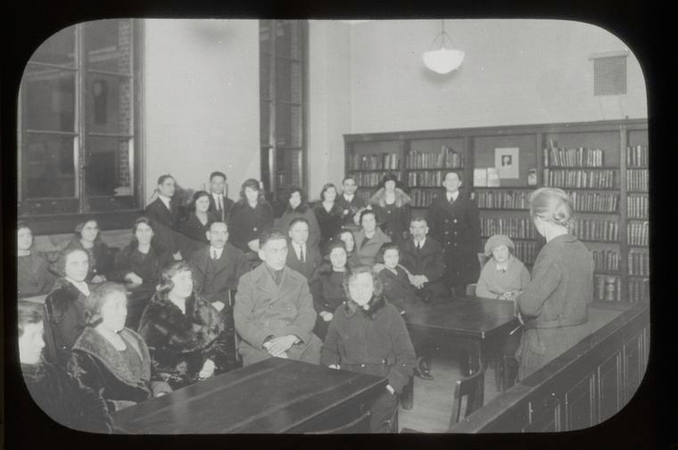 Adults sitting in a room while a teacher or librarian gives a lecture. 