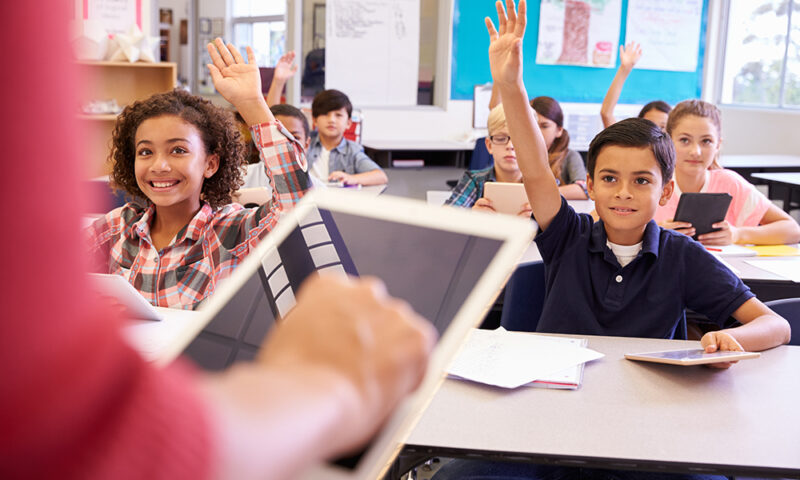 Elementary students raising their hands in classroom